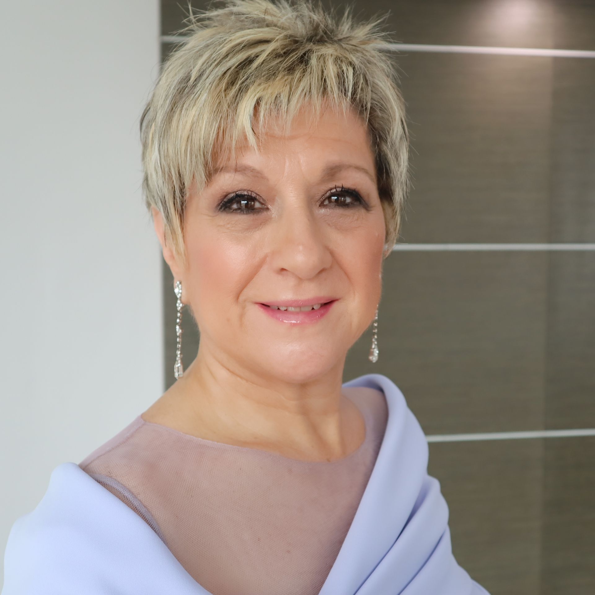 Una mujer con un top morado y pendientes sonríe a la cámara.