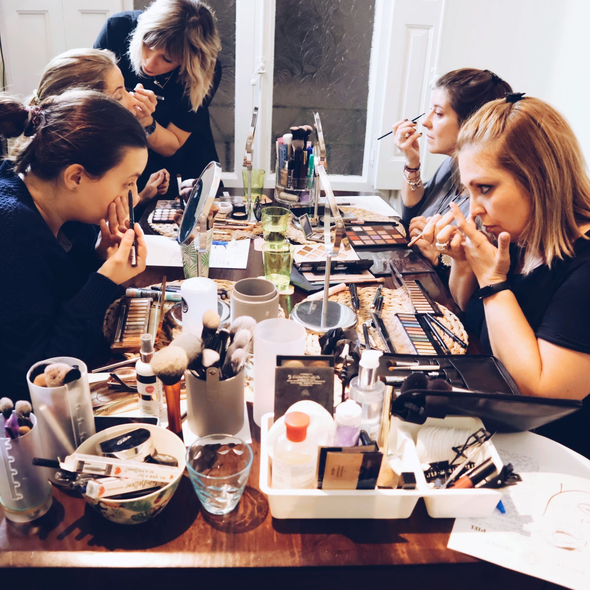 Un grupo de mujeres están sentadas en una mesa aplicándose maquillaje.