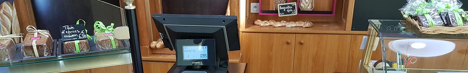 Un comptoir de caisse dans une boulangerie, avec un terminal de point de vente, des friandises emballées et des étagères en bois en arrière-plan.