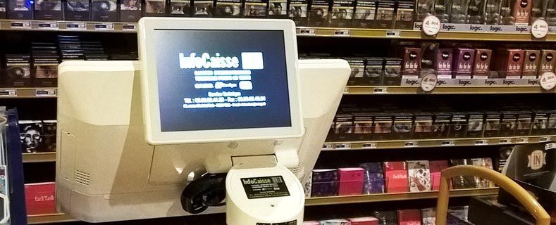 Un terminal de point de vente blanc affiche un écran de connexion InfoCaisse dans un magasin dont les rayons sont consacrés aux produits du tabac.