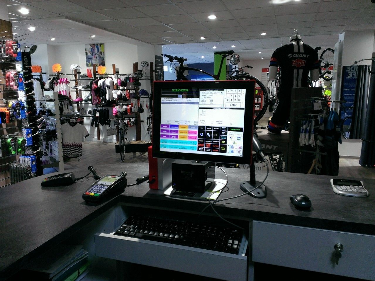 Un écran d'ordinateur, un clavier et un terminal de paiement à la caisse d'un magasin de sport.