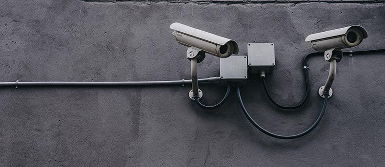 Deux caméras de sécurité fixées sur un mur gris, reliées par des fils noirs et deux boîtes de jonction.