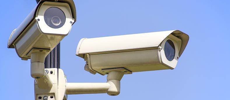 Deux caméras de sécurité extérieures blanches, fixées sur un poteau, se détachent sur un ciel bleu dégagé.