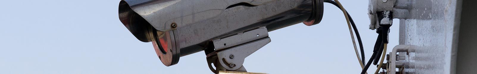 Une caméra de sécurité argentée fixée sur un poteau métallique se détachant sur un ciel bleu clair.