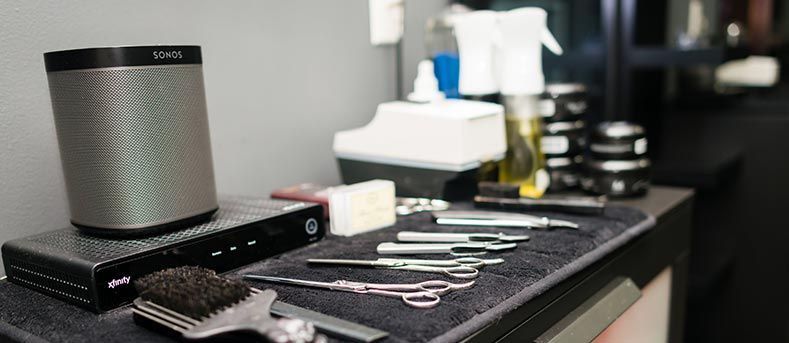 Un poste de travail de salon comprenant un haut-parleur, un décodeur câble, des ciseaux à cheveux, des peignes et des flacons de produits capillaires professionnels.