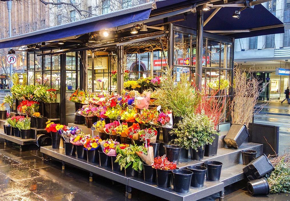 Un étal de fleurs de rue, abrité sous un auvent bleu, regorgeant de bouquets colorés, de verdure luxuriante et de plantes en pot.