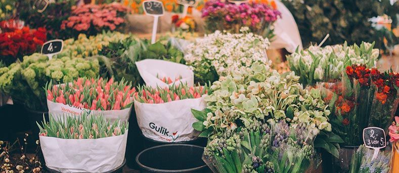 Un étalage coloré de fleurs variées et de tulipes emballées dans du papier, sur un marché.