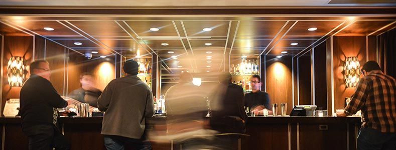 Des personnes debout à un bar en bois faiblement éclairé, avec un éclairage chaleureux et des appliques décoratives.