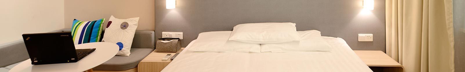 Une chambre d'hôtel moderne avec un lit blanc impeccablement fait, un petit coin bureau avec un ordinateur portable et des coussins décoratifs aux tons bleus.