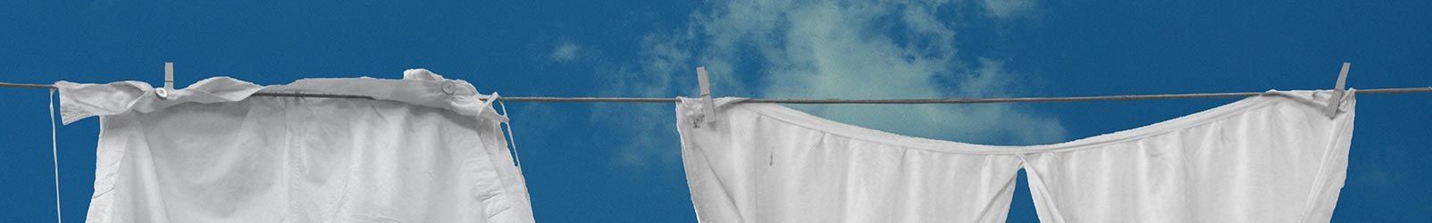 Deux rideaux blancs suspendus à une corde à linge se détachant sur un ciel bleu limpide.