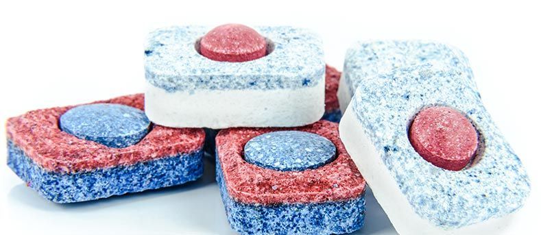 Un ensemble de pastilles de détergent pour lave-vaisselle colorées et multicouches, avec des segments bleus, rouges et blancs sur fond blanc.