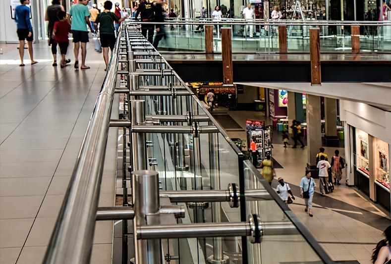 Les clients déambulent dans un centre commercial lumineux à plusieurs niveaux, doté de balustrades métalliques surplombant l'étage inférieur.