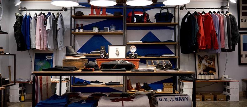 Un présentoir de vêtements en magasin comprenant des chemises et des vestes suspendues, des accessoires sur des étagères et des vêtements pliés sur une table centrale.