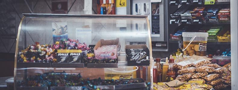 Vitrine remplie de divers en-cas et friandises à l'intérieur d'un magasin, avec d'autres produits sur des étagères en arrière-plan.