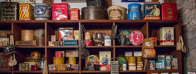 Une grille d'étagères remplies de boîtes en fer, de récipients et d'articles ménagers anciens, disposées comme dans une épicerie d'antiquités.