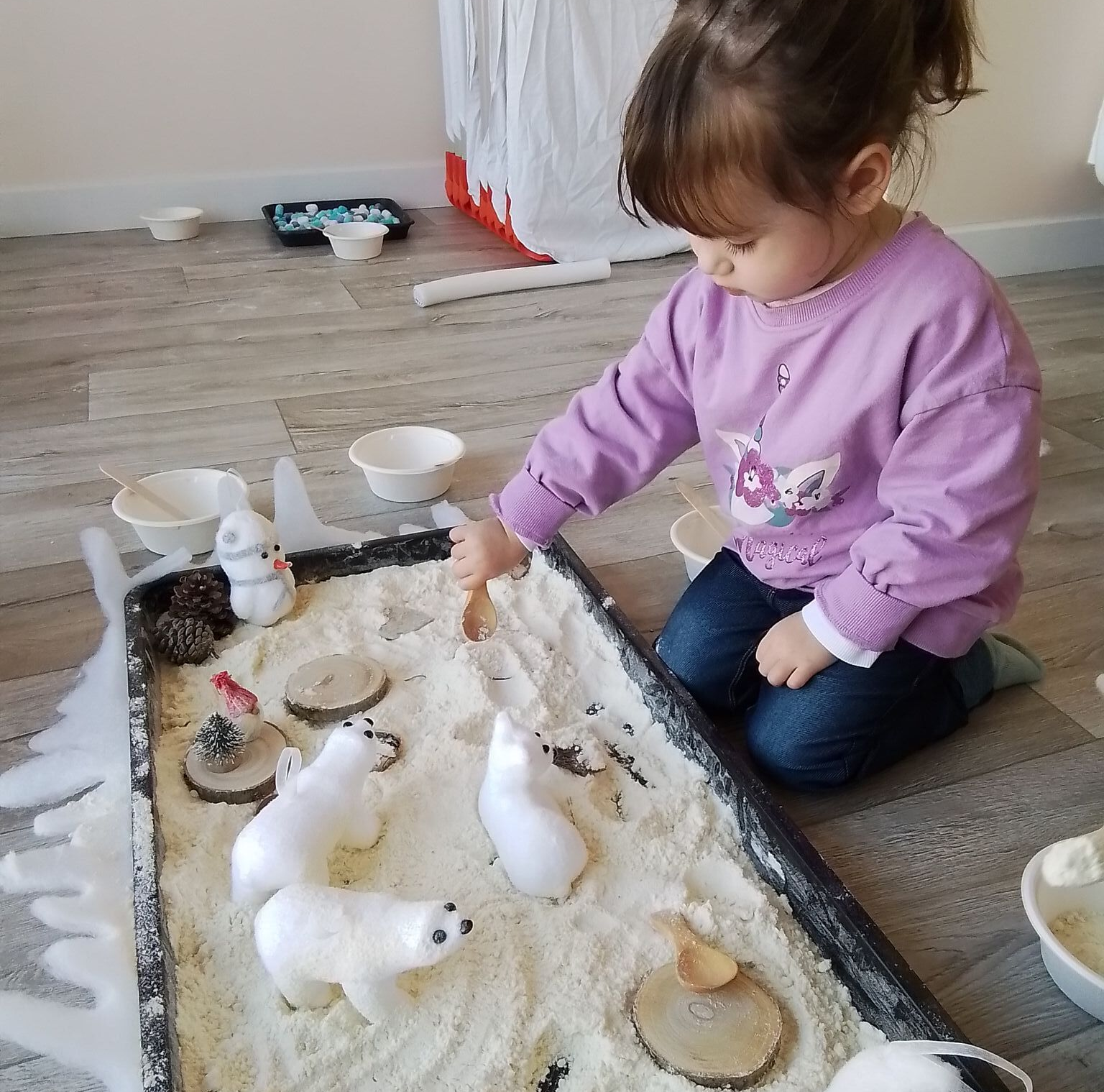 Une fillette joue avec des ours polaires en peluche sur un plateau rempli de matière sensorielle blanche, comme de la neige.
