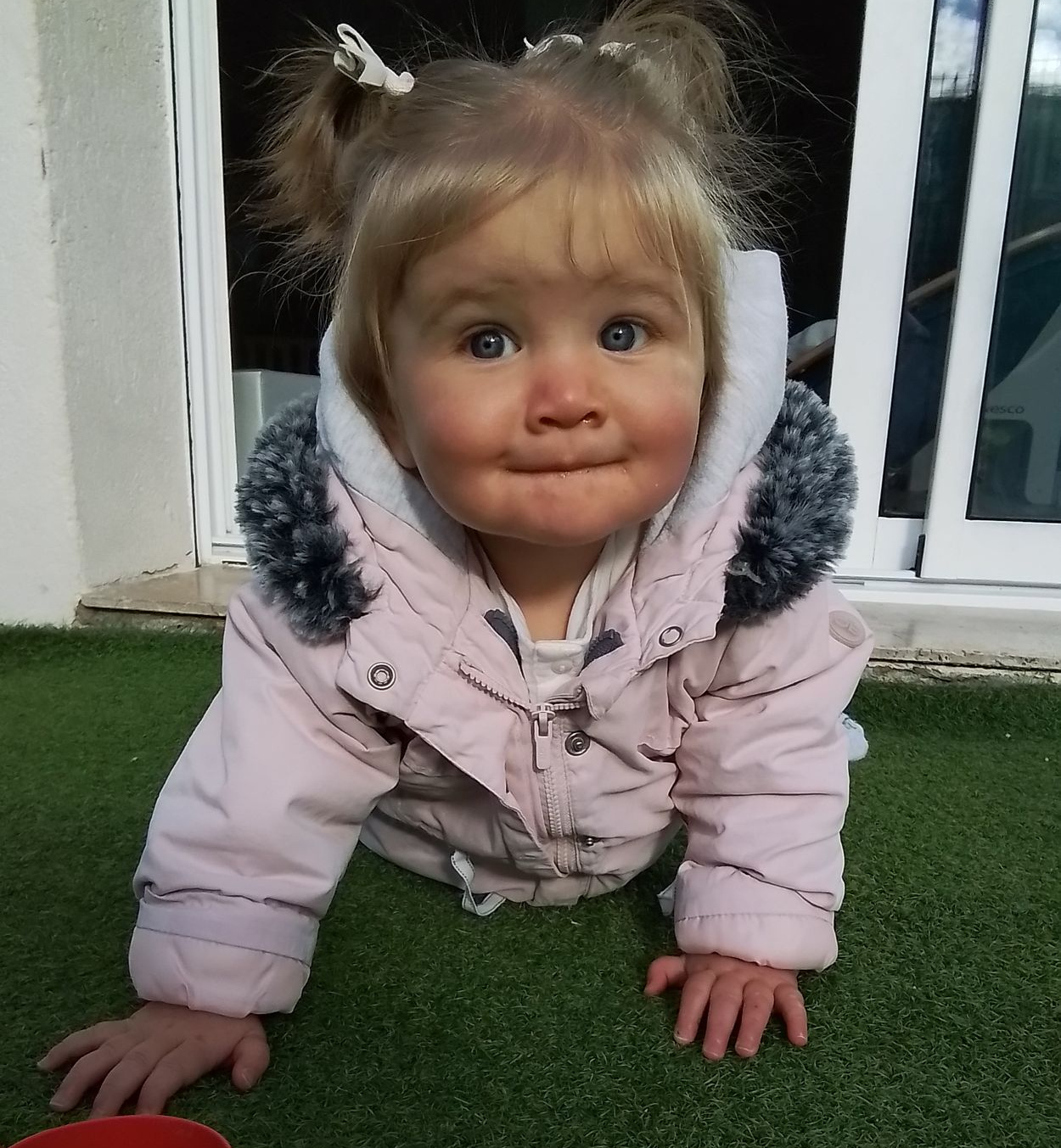 Enfant en veste rose rampant sur l'herbe verte, regardant l'objectif.
