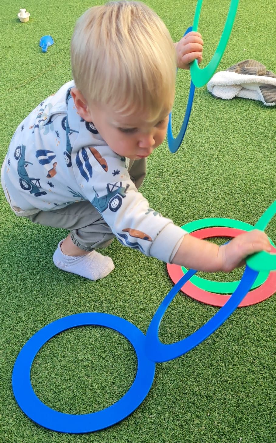 Un jeune enfant joue à un jeu de lancer d'anneaux colorés sur un sol vert.