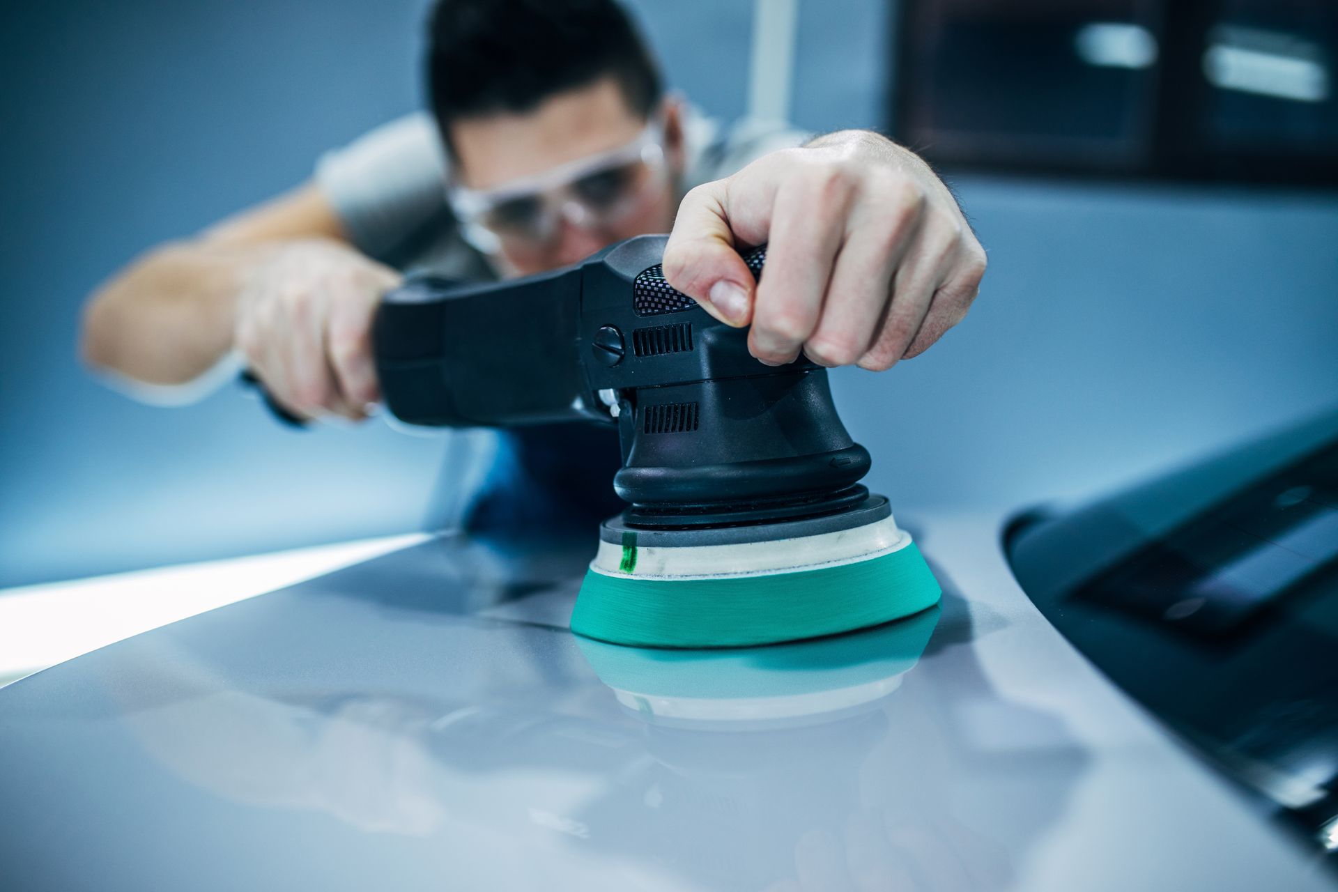 Personne polissant une voiture avec une polisseuse électrique. Voiture blanche dans un garage.