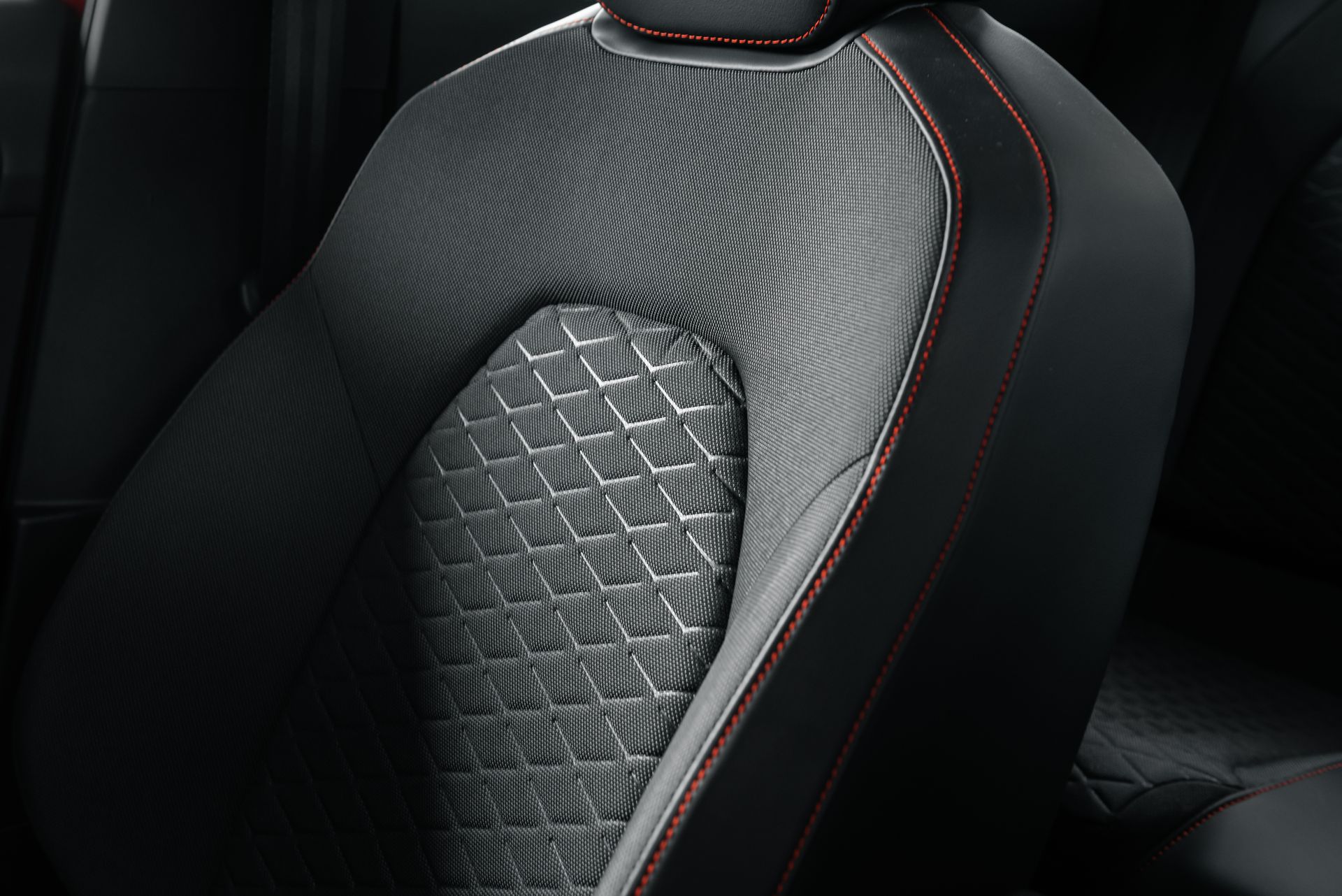 Gros plan d'un siège auto noir avec des inserts gris texturés et des coutures rouges.