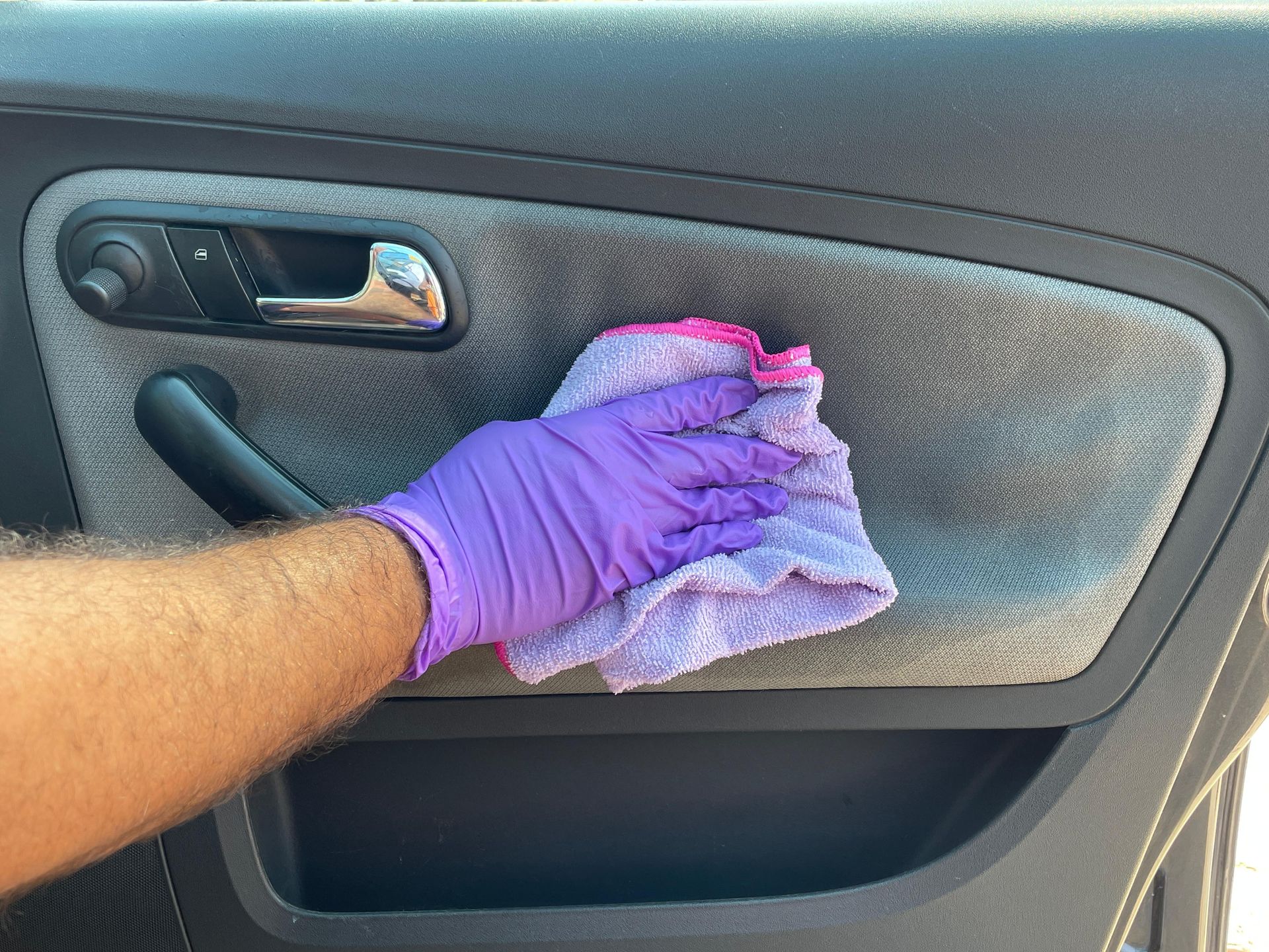 Une main gantée essuie le panneau de portière d'une voiture avec un chiffon rose et blanc.