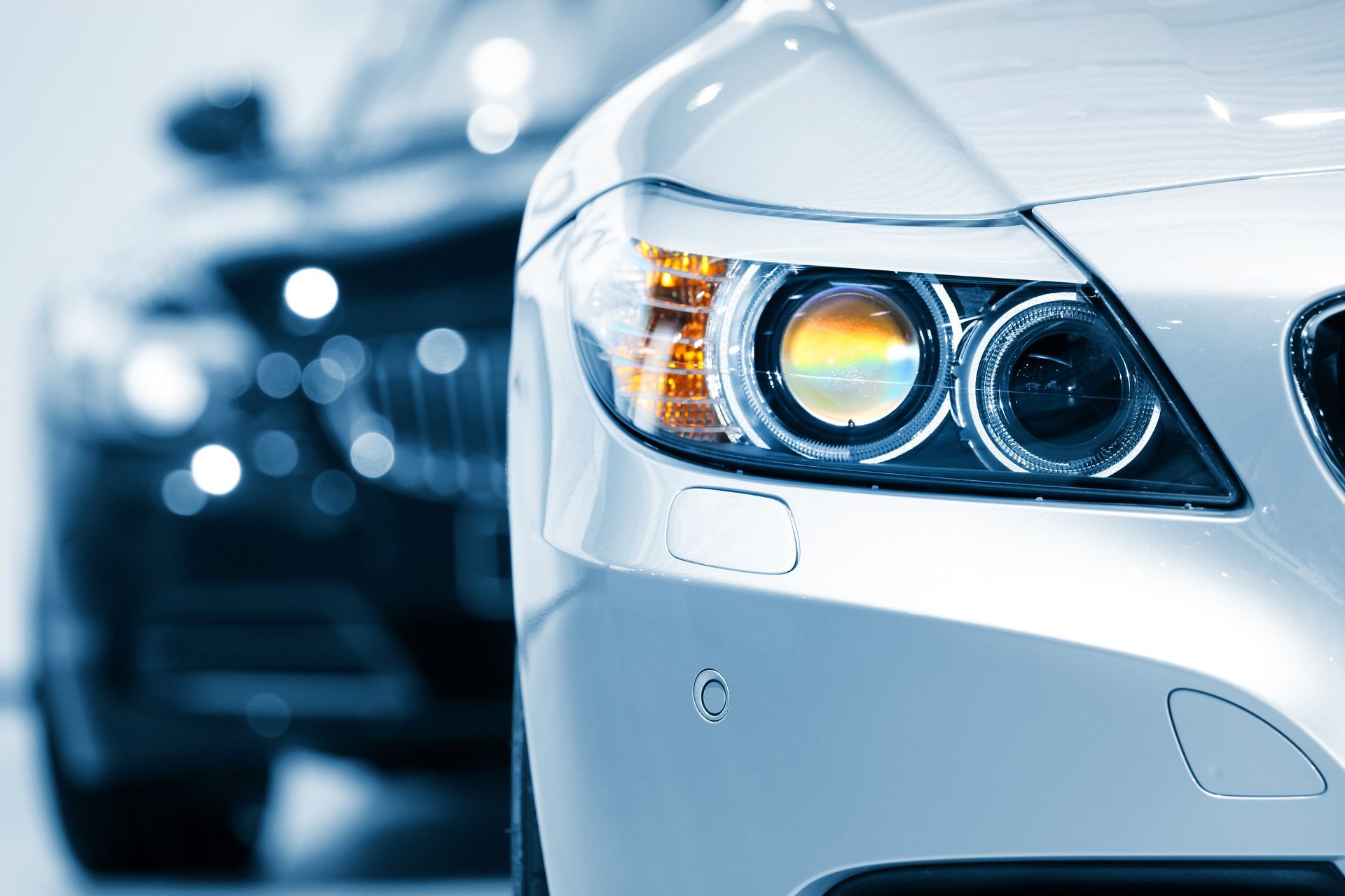 Gros plan d'un phare de voiture argenté, avec une voiture noire floue en arrière-plan.