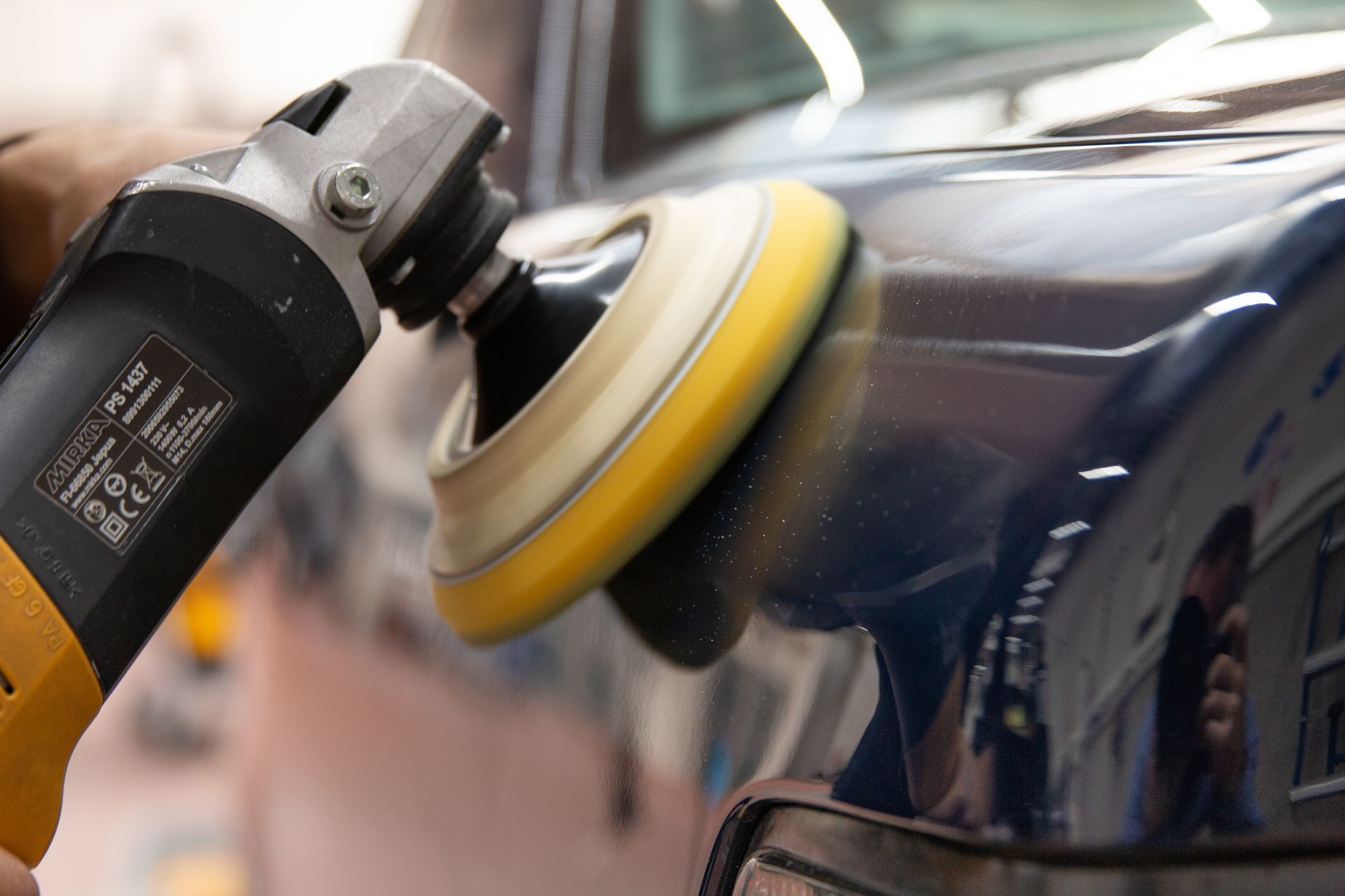 Une personne polissant une voiture bleu foncé avec une polisseuse électrique jaune et noire.