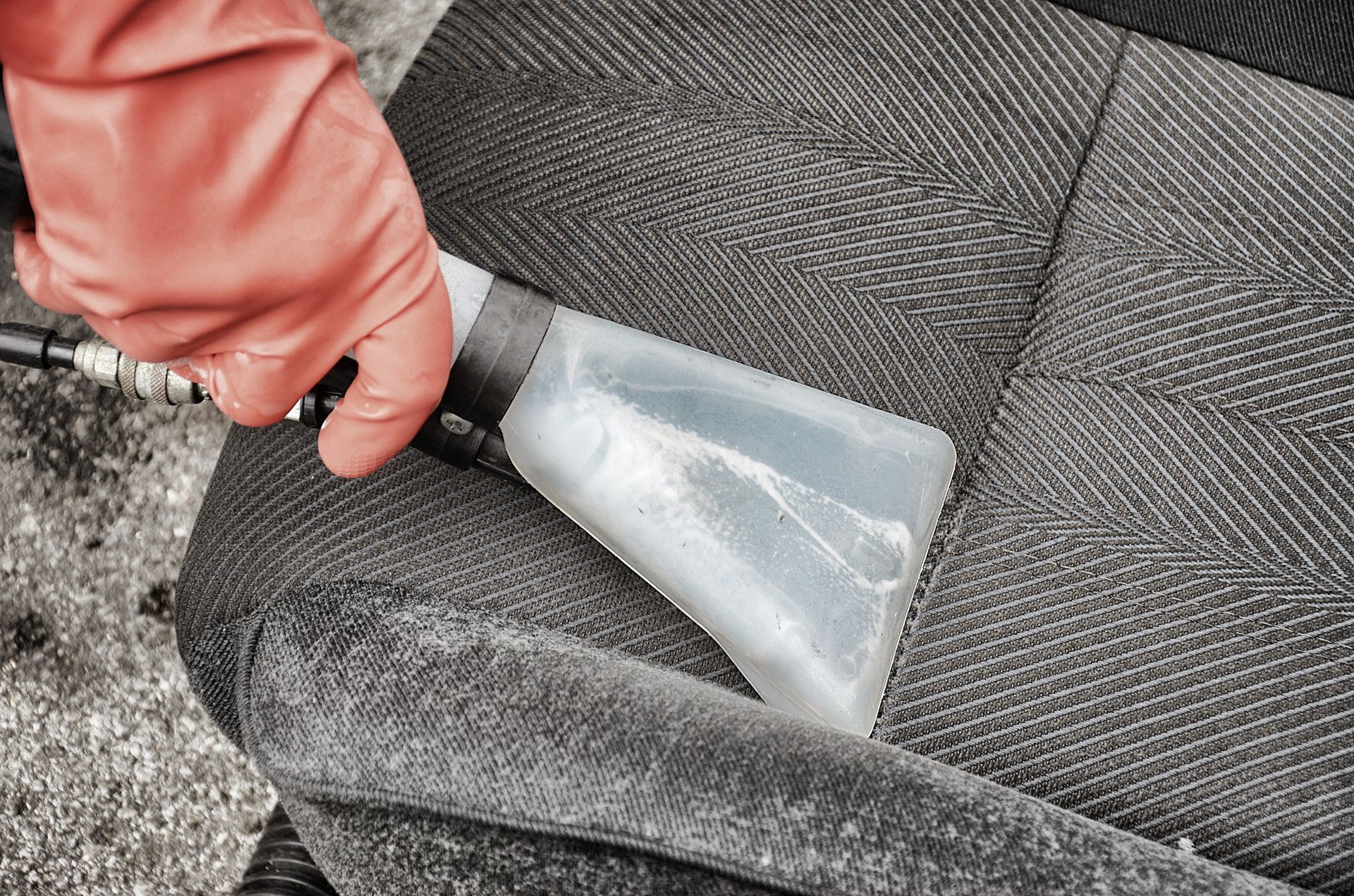 Main gantée de rouge utilisant un outil de nettoyage sur un siège de voiture, avec de l'eau visible.