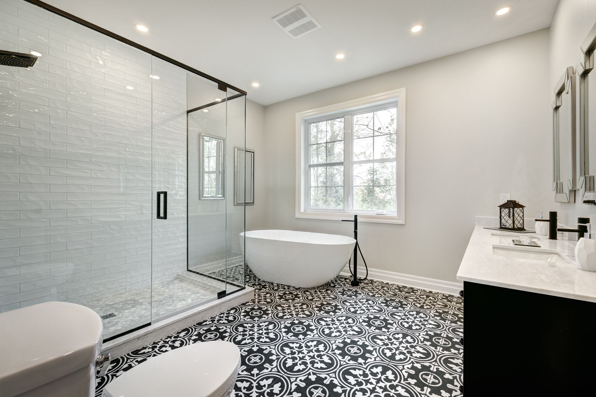 Baño moderno con azulejos estampados en blanco y negro, ducha de vidrio, bañera blanca y tocador negro.