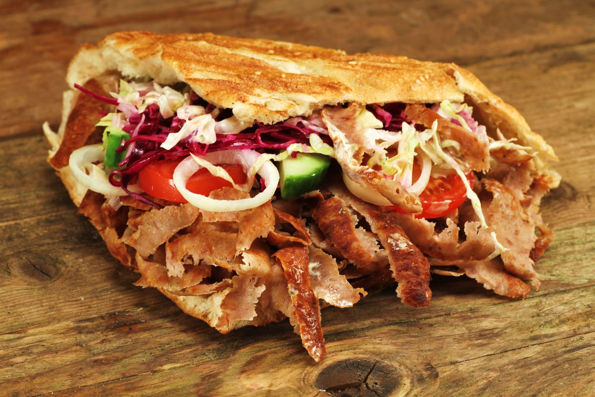 Spiesse mit gegrilltem Fleisch und Gemüse auf einem schwarzen Teller mit einer kleinen Schüssel roter Sosse.