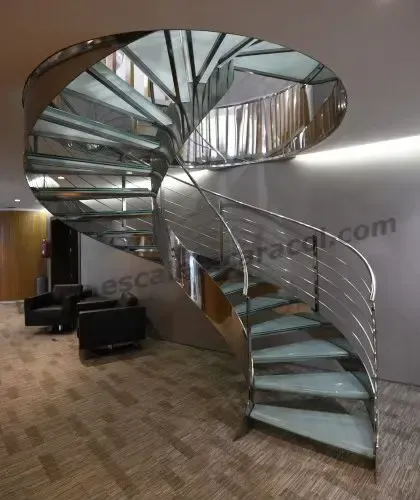 Una escalera de caracol con barandilla de acero inoxidable y escalones de cristal.
