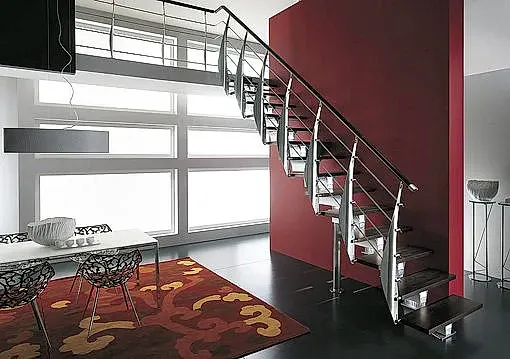 Una escalera en una sala de estar con una pared roja y una alfombra.