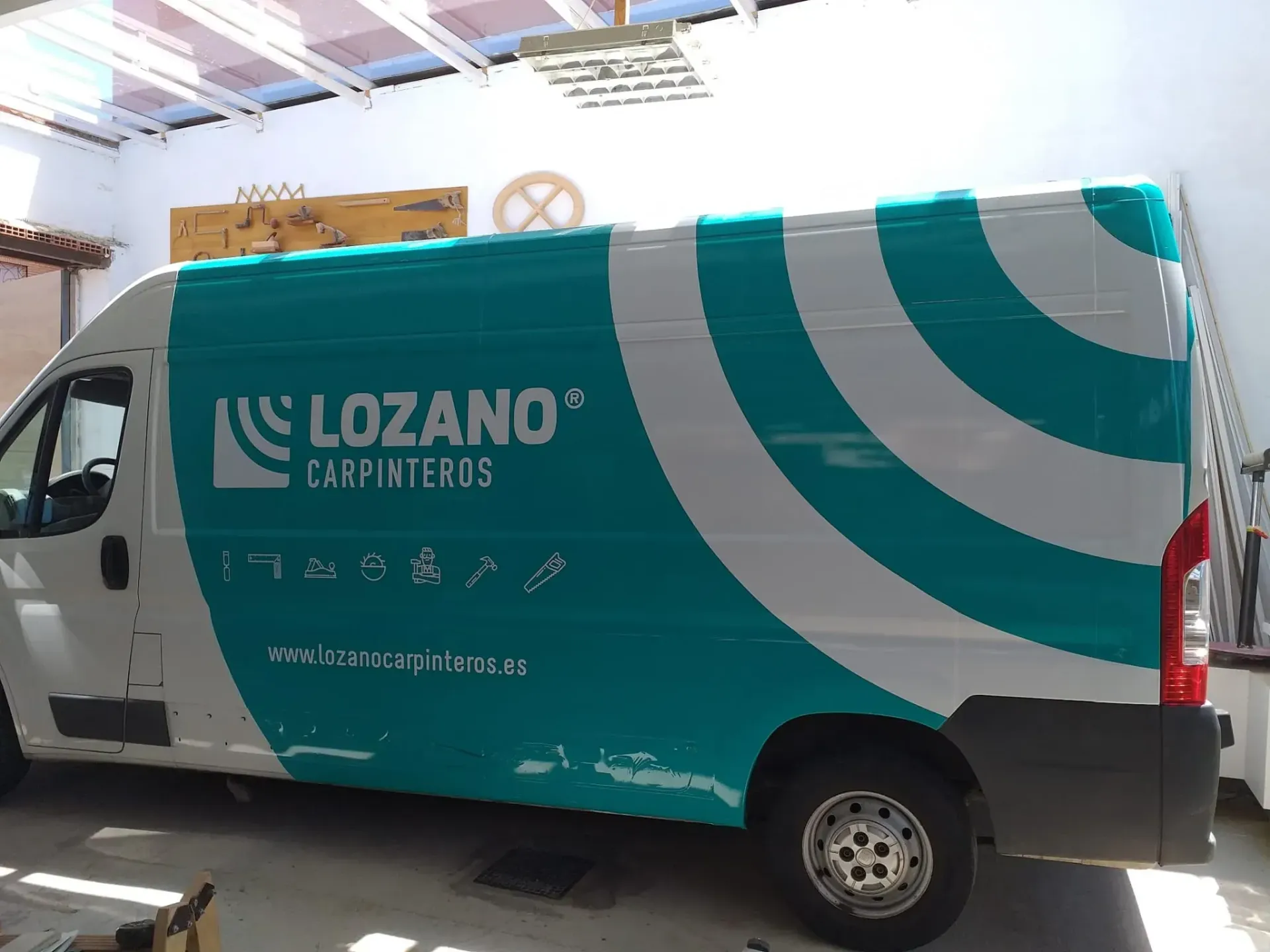 Un técnico con casco azul y chaleco reflectante habla por teléfono mientras trabaja en un ordenador portátil en un parque eólico.