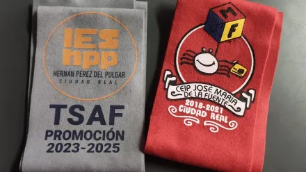 Dos camisetas dobladas: una gris con el logotipo naranja de TSU HPP y otra roja con una mascota de dibujos animados y letras blancas.