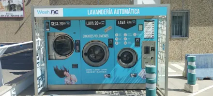 Lavanderías de autoservicio de color turquesa al aire libre, con ranuras para monedas y un pasillo soleado en las cercanías.