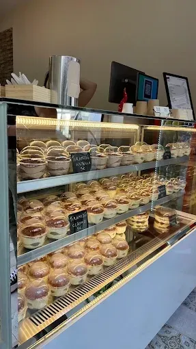Vitrina de panadería llena de pasteles y galletas variadas bajo cristal en una cafetería.