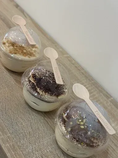 Tres copas de postre con tapas transparentes y cucharas, dispuestas en diagonal sobre una mesa texturizada.