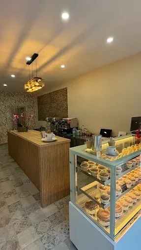 Pequeña cafetería moderna de postres con mostrador de madera, vitrina de pasteles y cálida iluminación colgante.