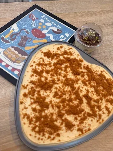 Tiramisú servido en un bol transparente, espolvoreado con cacao en polvo, sobre la mesa de una cafetería.