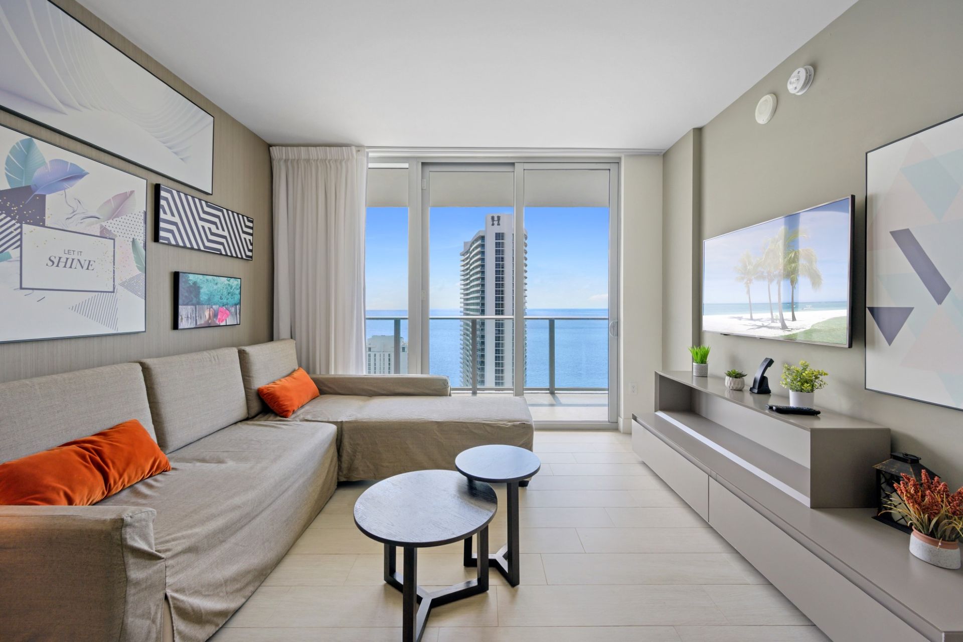 A living room with a couch , two tables , a television and a balcony overlooking the ocean.