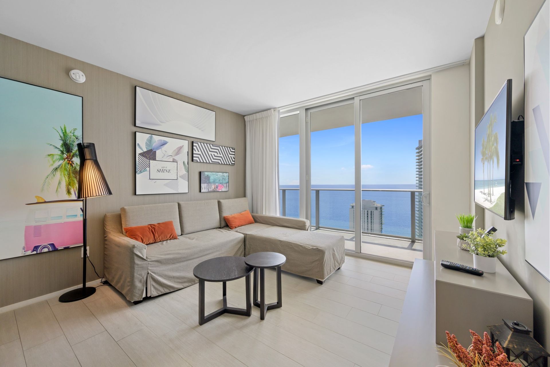A living room with a couch , two tables , a television and a balcony overlooking the ocean.