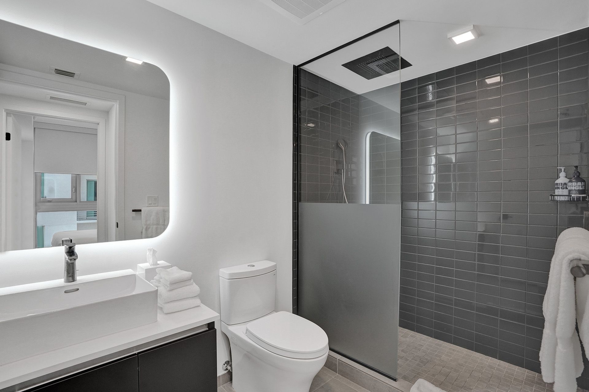 A bathroom with a toilet , sink , mirror and walk in shower.