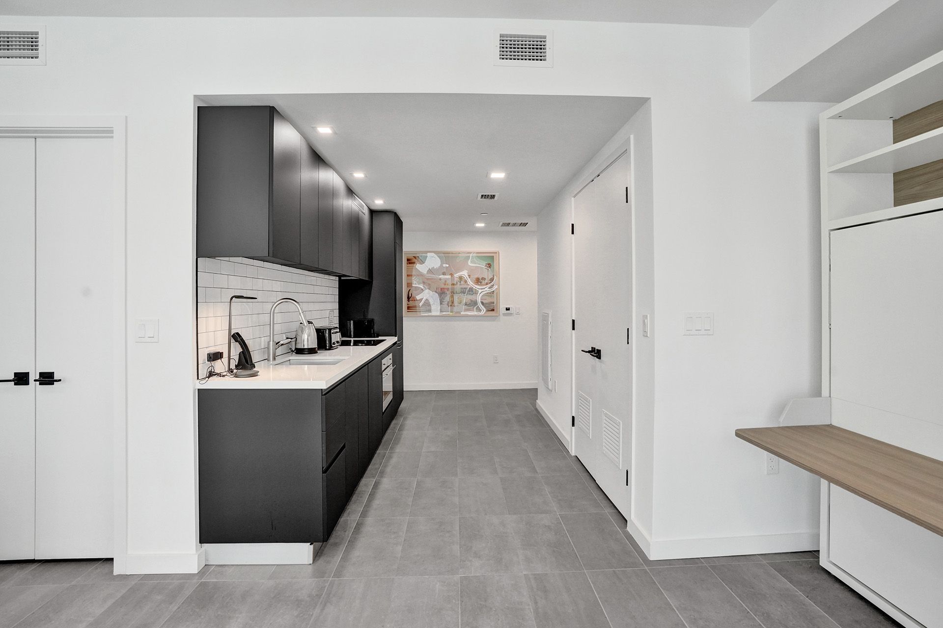 A kitchen with black cabinets and white counter tops in a hallway.
