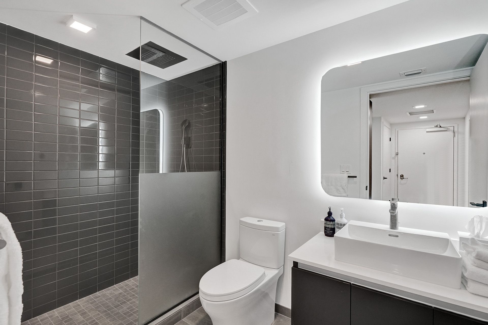 A bathroom with a toilet , sink , mirror and walk in shower.