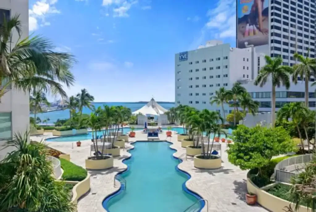 A large swimming pool is surrounded by palm trees and a building.