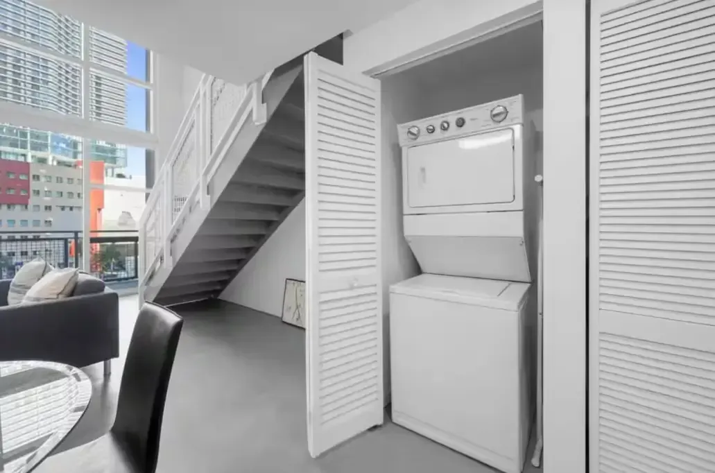 A washer and dryer are stacked on top of each other in a closet under a staircase.