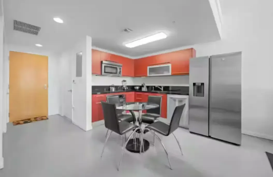 A kitchen with red cabinets , a stainless steel refrigerator , a table and chairs.