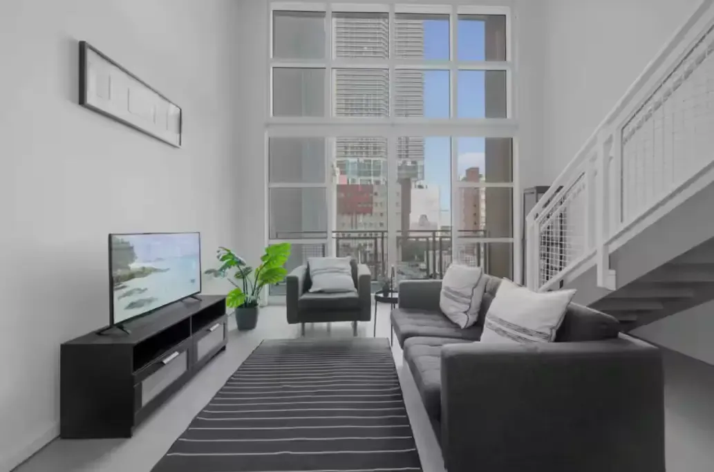 A living room with a couch , chair , television and stairs.