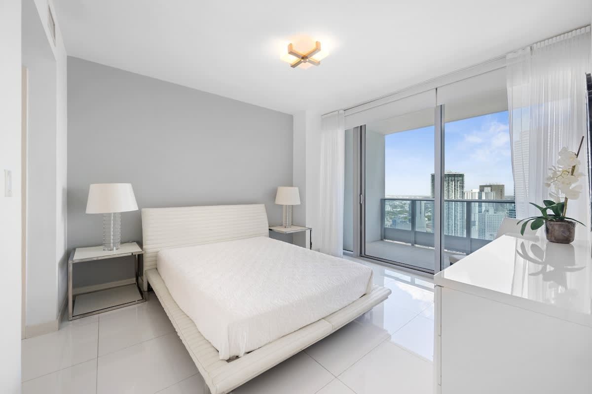 A bedroom with a bed , dresser , lamps and a balcony.