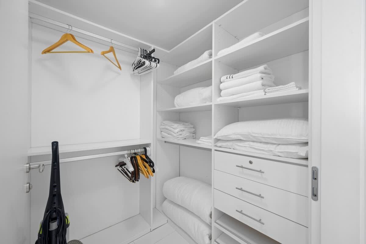 A walk in closet filled with clothes and a vacuum cleaner.